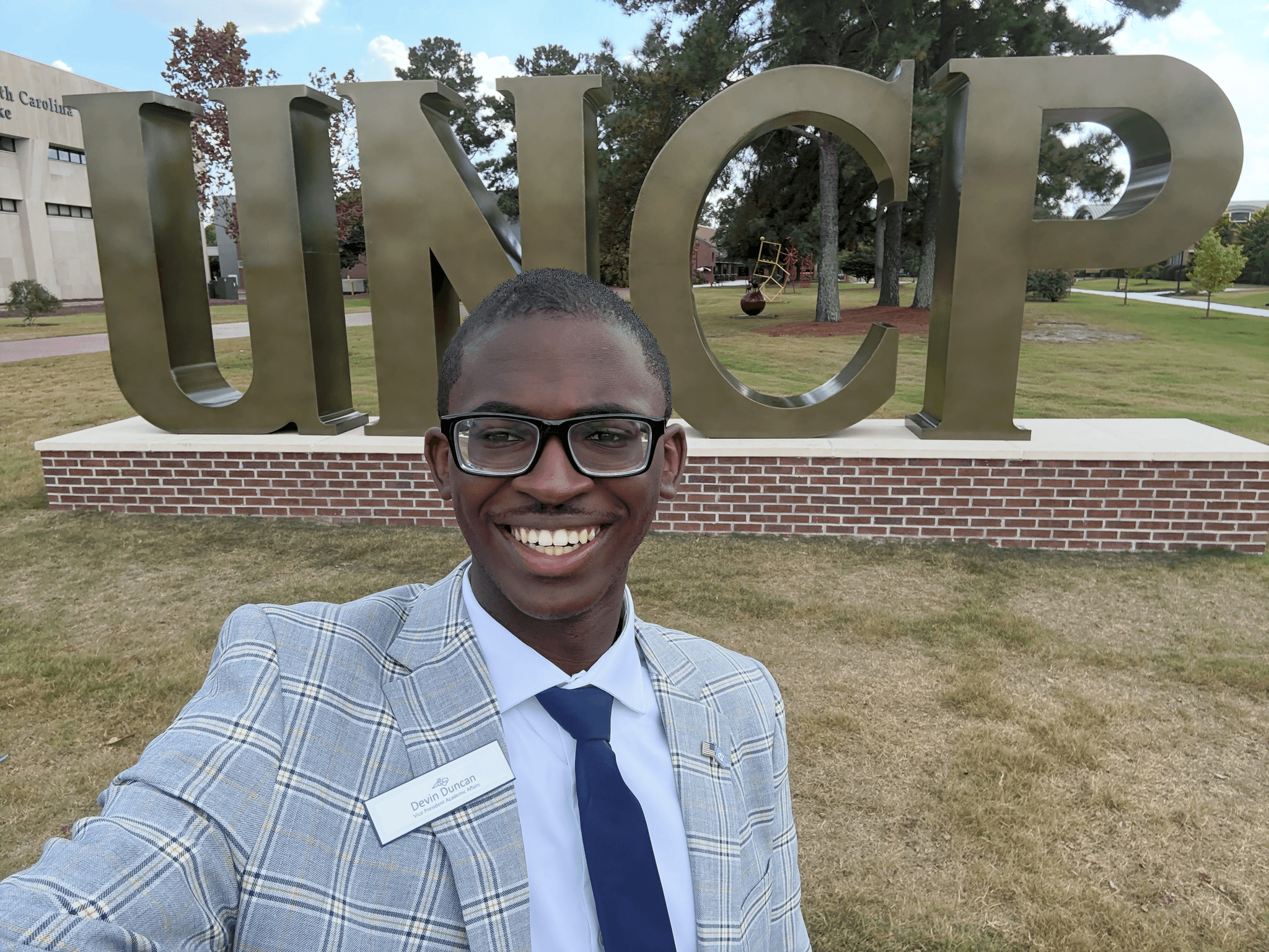 Devin wearing a suit in front of a UNCP sign